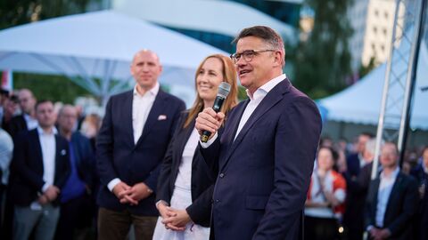Ministerpräsident Rhein steht gemeinsam mit Landtagspräsidentin Astrid Wallmann und Europaminister Pentz vor Publikum und spricht ins Mikrofon.