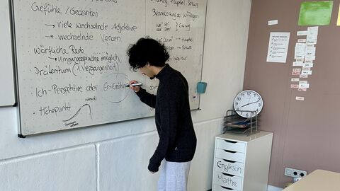 Ein Jugendlicher steht an einem Whiteboard und schreibt etwas darauf.