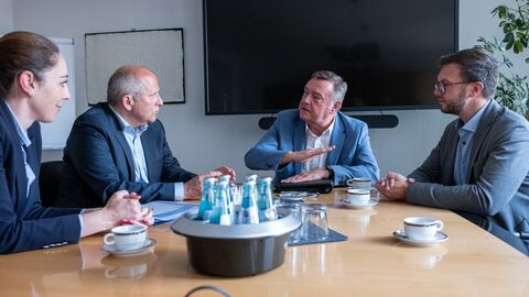 Drei Männer und eine Frau sitzen an einem Tisch und unterhalten sich.